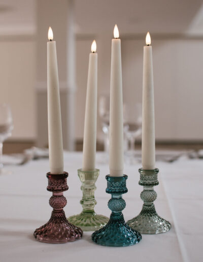 Four taper candles in coloured glass candlesticks